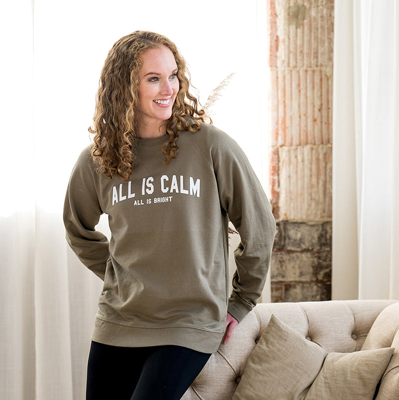 Woman smiling in sage green All is Calm crewneck sweatshirt.