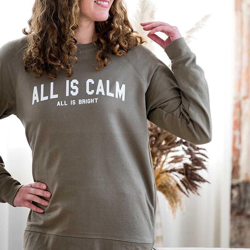 Woman in sage green All is Calm crewneck sweatshirt.