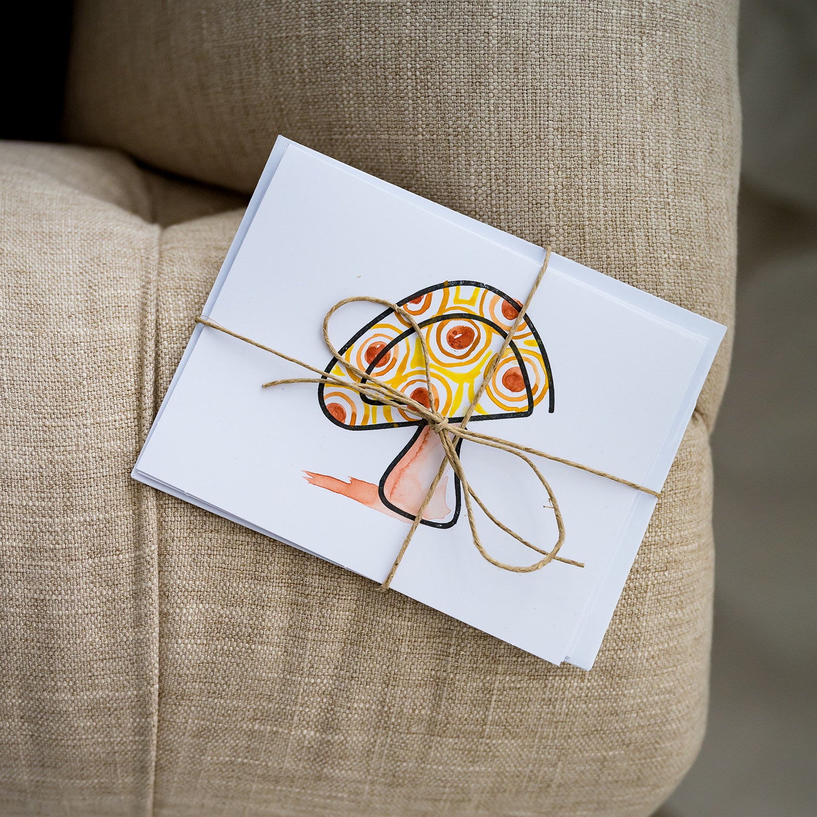 Watercolor and stamped note card of mushroom wrapped in twine on fabric couch.