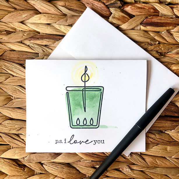 Watercolor and stamped note card of green candle wrapped in twine on basket pattern with pen.