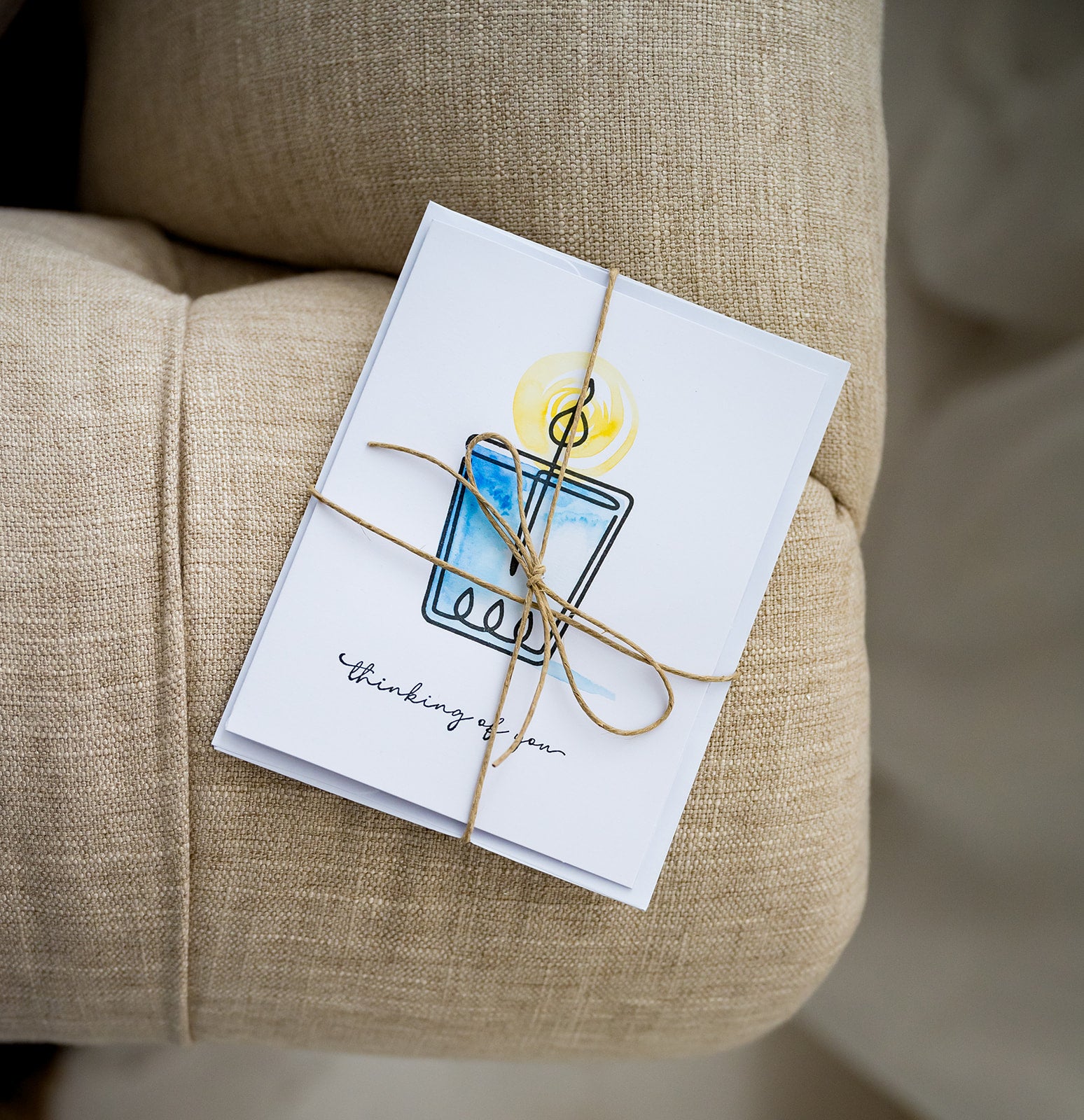 Watercolor and stamped note card of candle wrapped in twine on fabric couch.