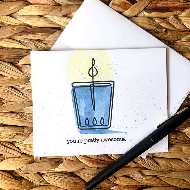 Watercolor and stamped note card of blue candle wrapped in twine on basket pattern with pen.