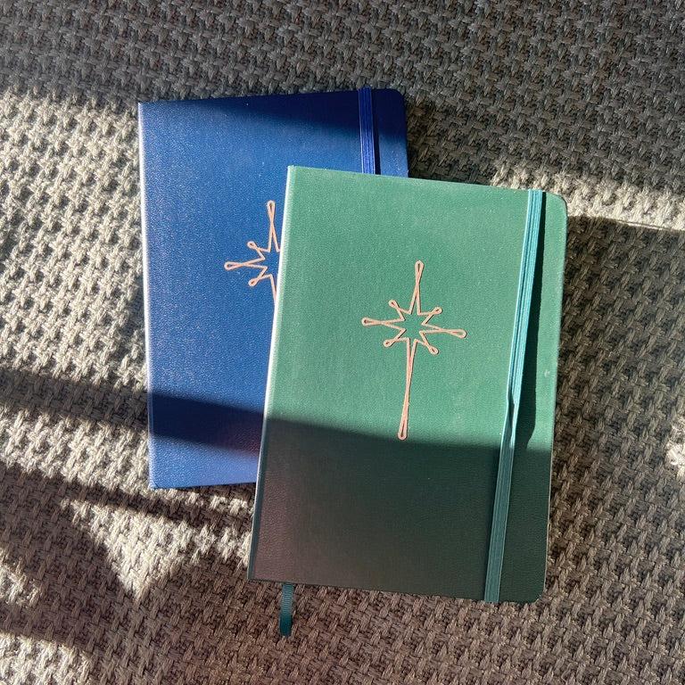 Navy and green notebooks with gold star on green blanket. 