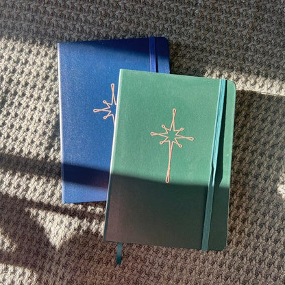 Navy and green notebooks with gold star on green blanket. 