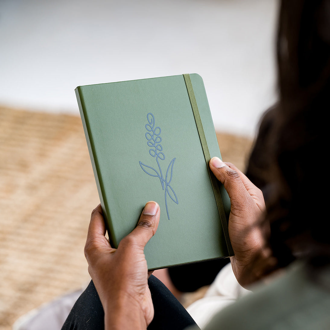 Woman holding green notebook with lavender design on the cover.