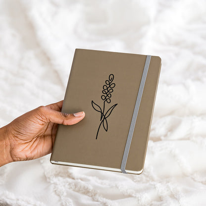 Woman holding taupe notebook with lavender design on the cover.