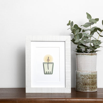 Black single-line art of green and yellow candle on white, framed in wood, displayed near vase of eucalyptus on wooden shelf.