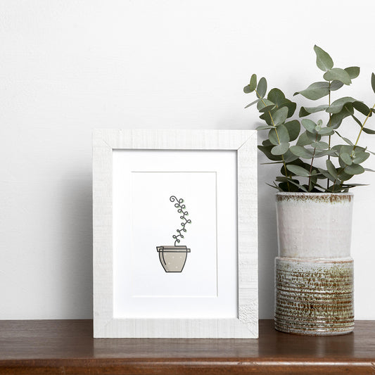 Black single-line art of green succulent in brown pot on white, framed in wood, displayed near vase of eucalyptus on wooden shelf.