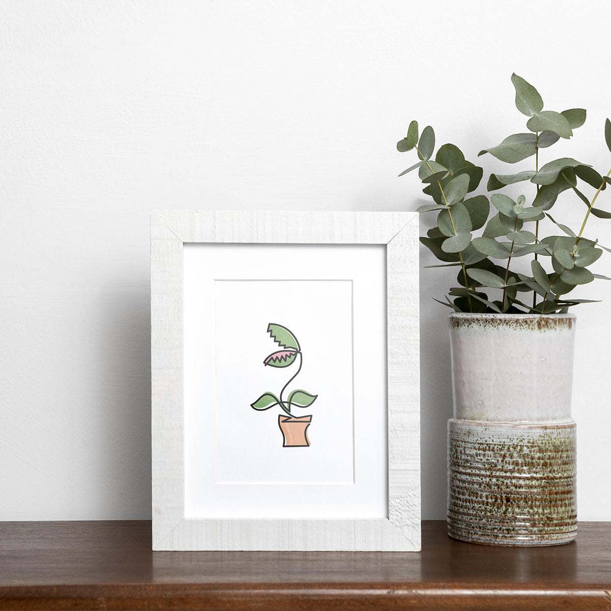 Black single-line art of green venus fly trap plant in clay pot on white, framed in wood, displayed near vase of eucalyptus on wooden shelf.