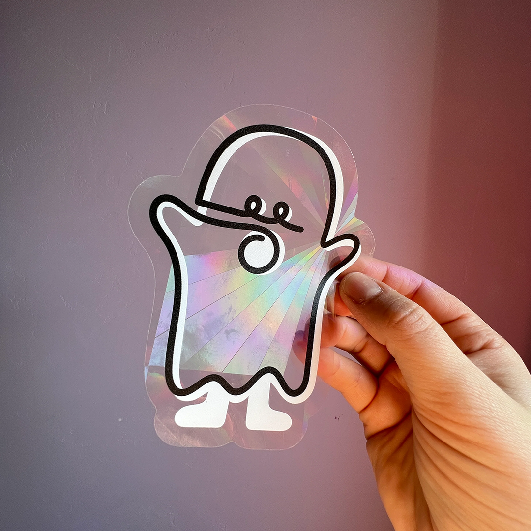 Hand holding rainbow sun catcher sticker with ghost on purple wall.