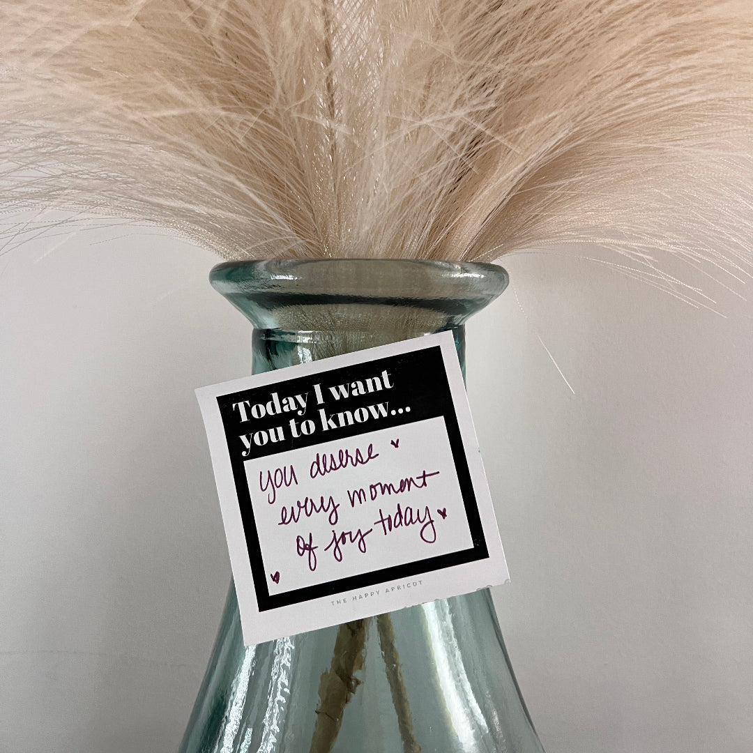 Note written on black and white sticky note on vase of feathers.