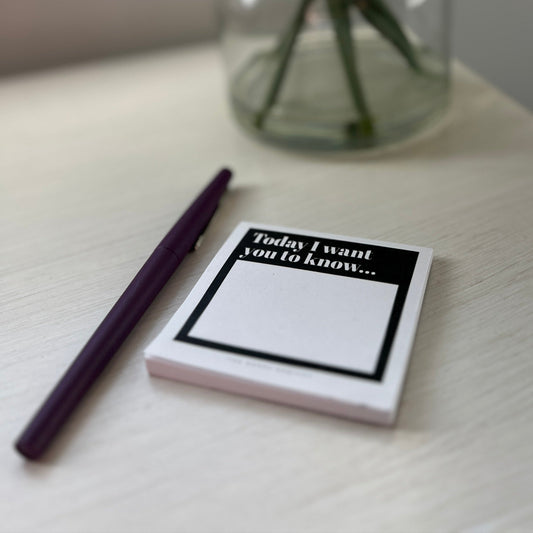 Black and white pad of sticky notes with black pen next to vase.