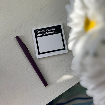 Overhead image of black and white pad of sticky notes with purple pen. 